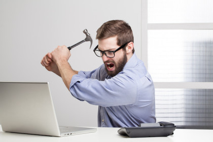 Furious businessman destroying his laptop with a hammer.